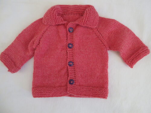 %%Handknit Collared Infant Sweater%%, Made and donated by Anne Morris; Approximate size 6-9 months; Washable DK weight yarn; 75% acrylic and 25% wool; Coral with purple buttons.